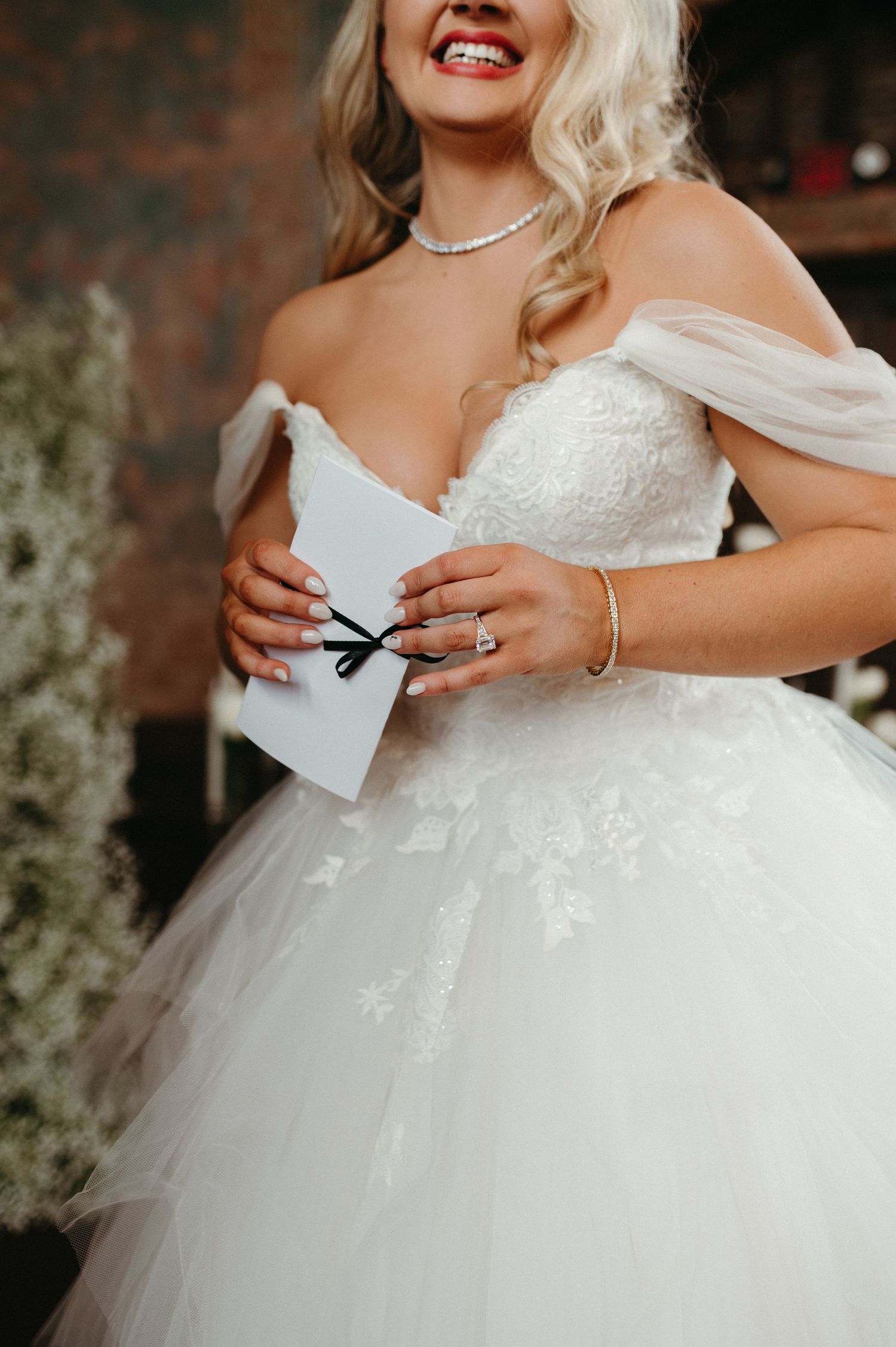 Close-up of a bride in a white tulle gown holding a letter while wearing delicate jewelry.