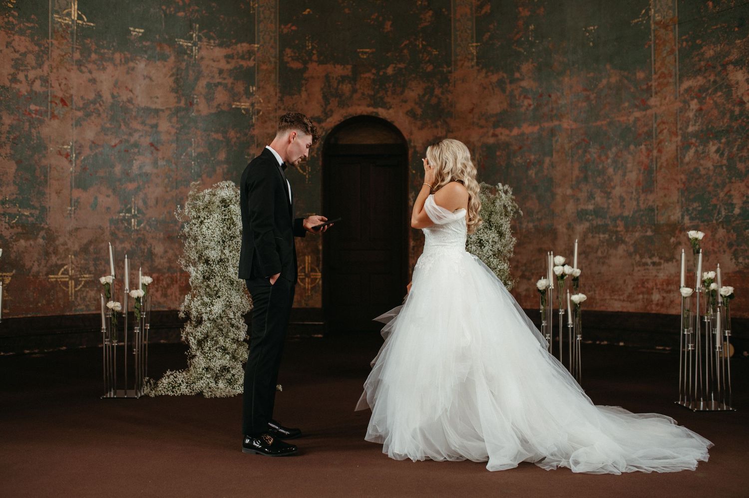 Newlyweds share a moment in a vintage church with candlelit aisle decorations and baby's breath arrangements.