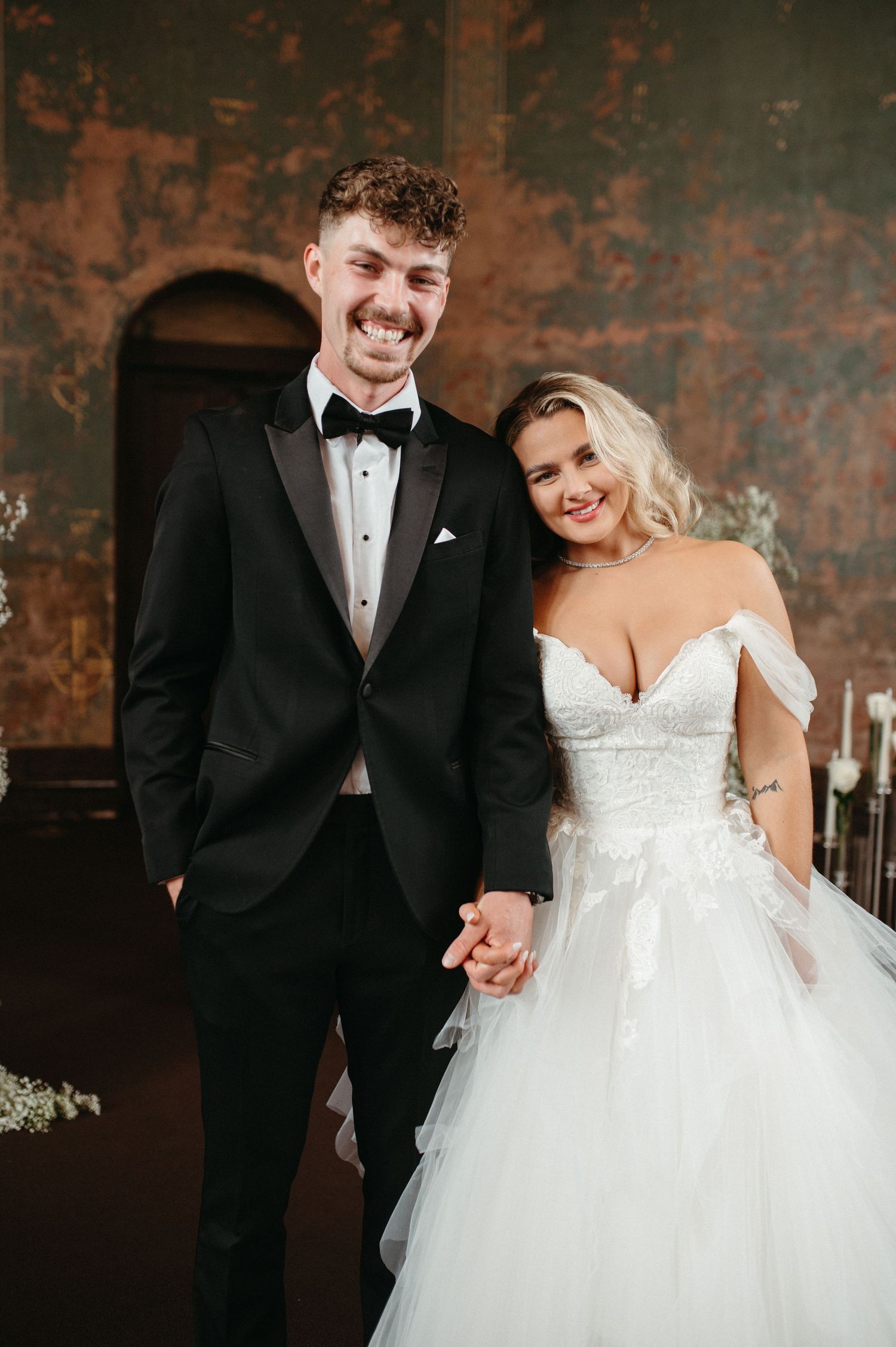 Joyful wedding portrait in front of rustic walls with classic black and white attire.