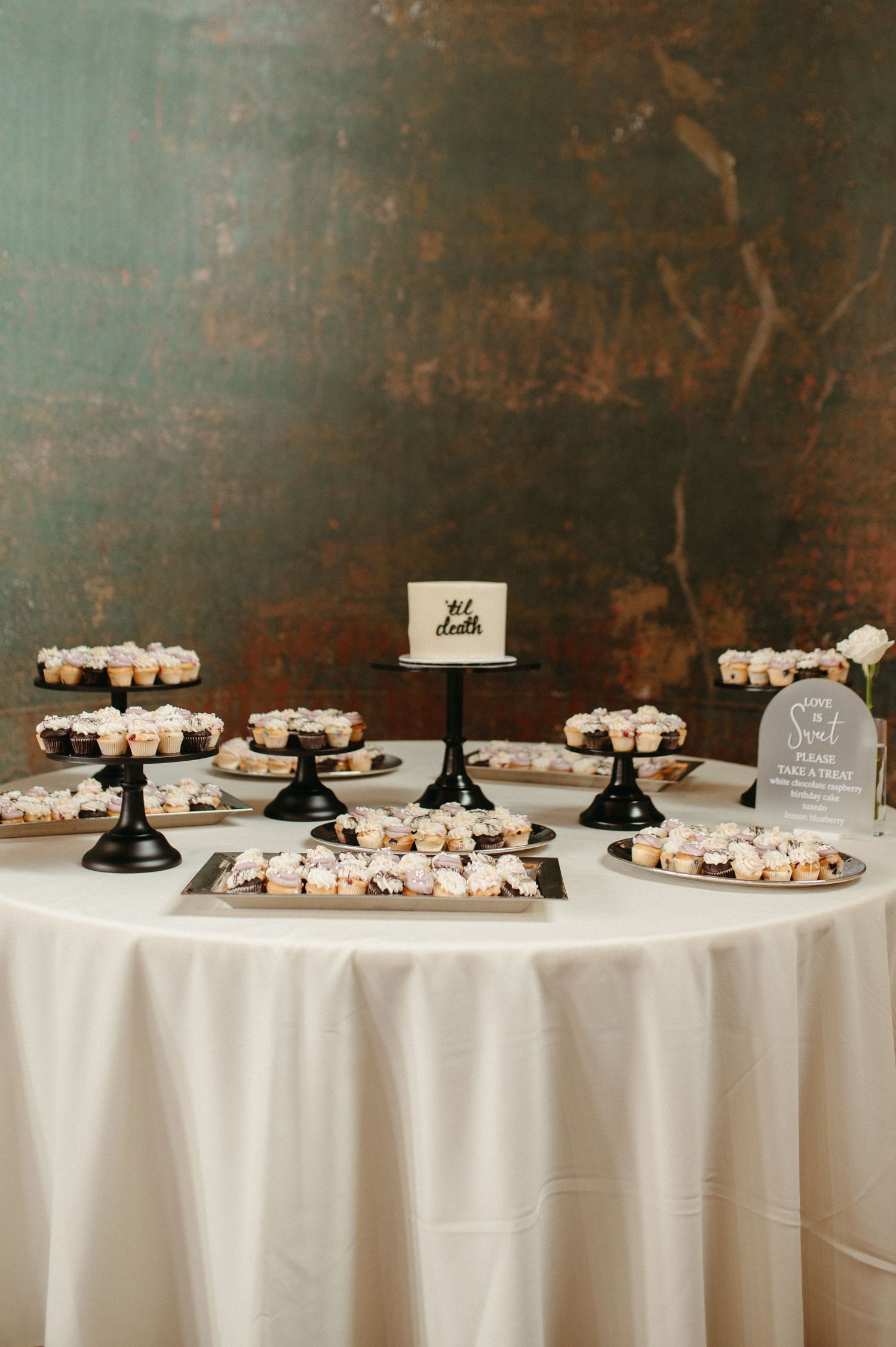 An elegant dessert table with multiple tiers of sweets displayed on black pedestals against a dark wall.