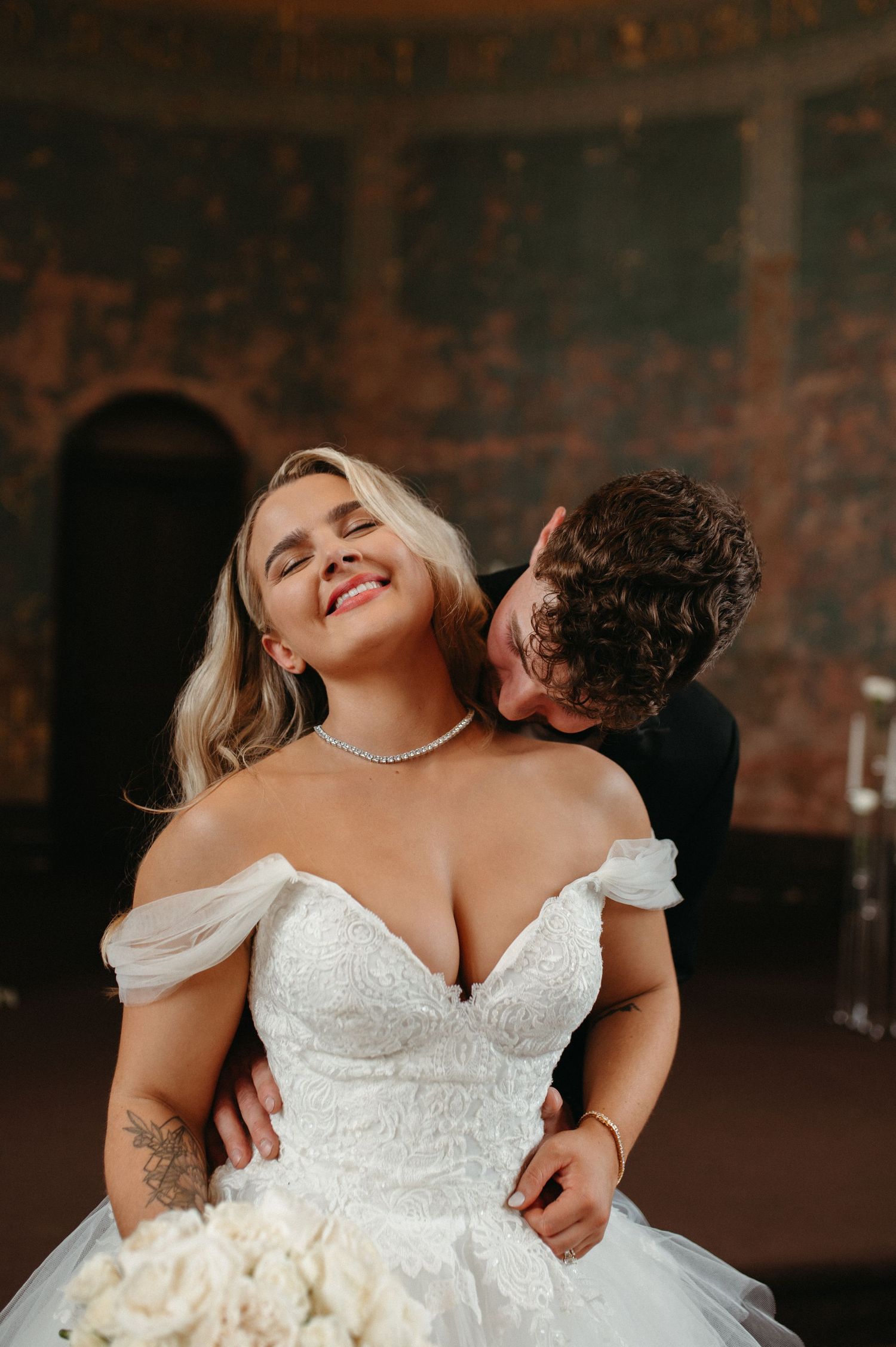A romantic moment between newlyweds as they embrace, with the bride wearing an off-shoulder white lace wedding gown.