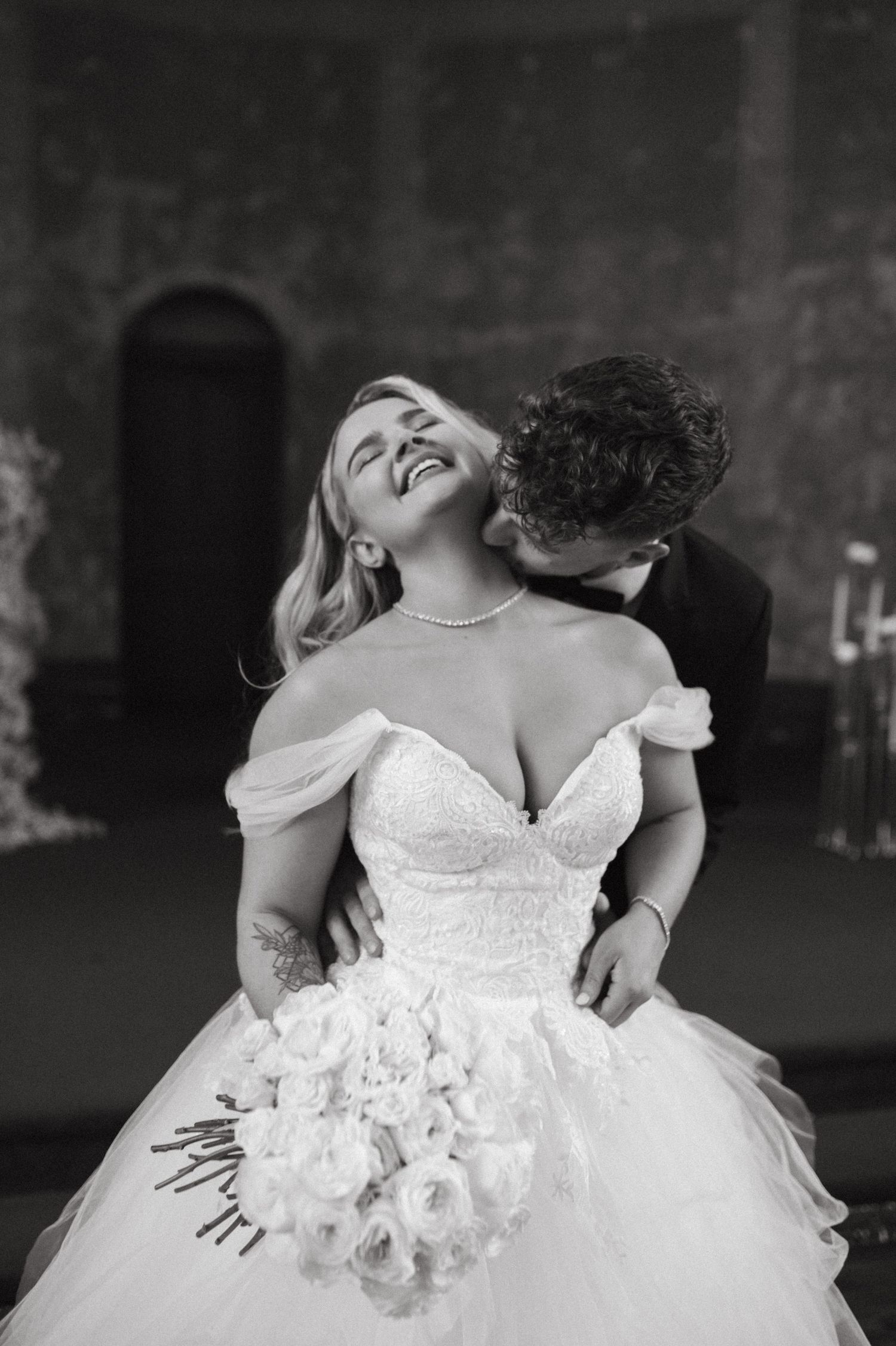 Joyful wedding moment captured in black and white showing the bride holding a white rose bouquet.