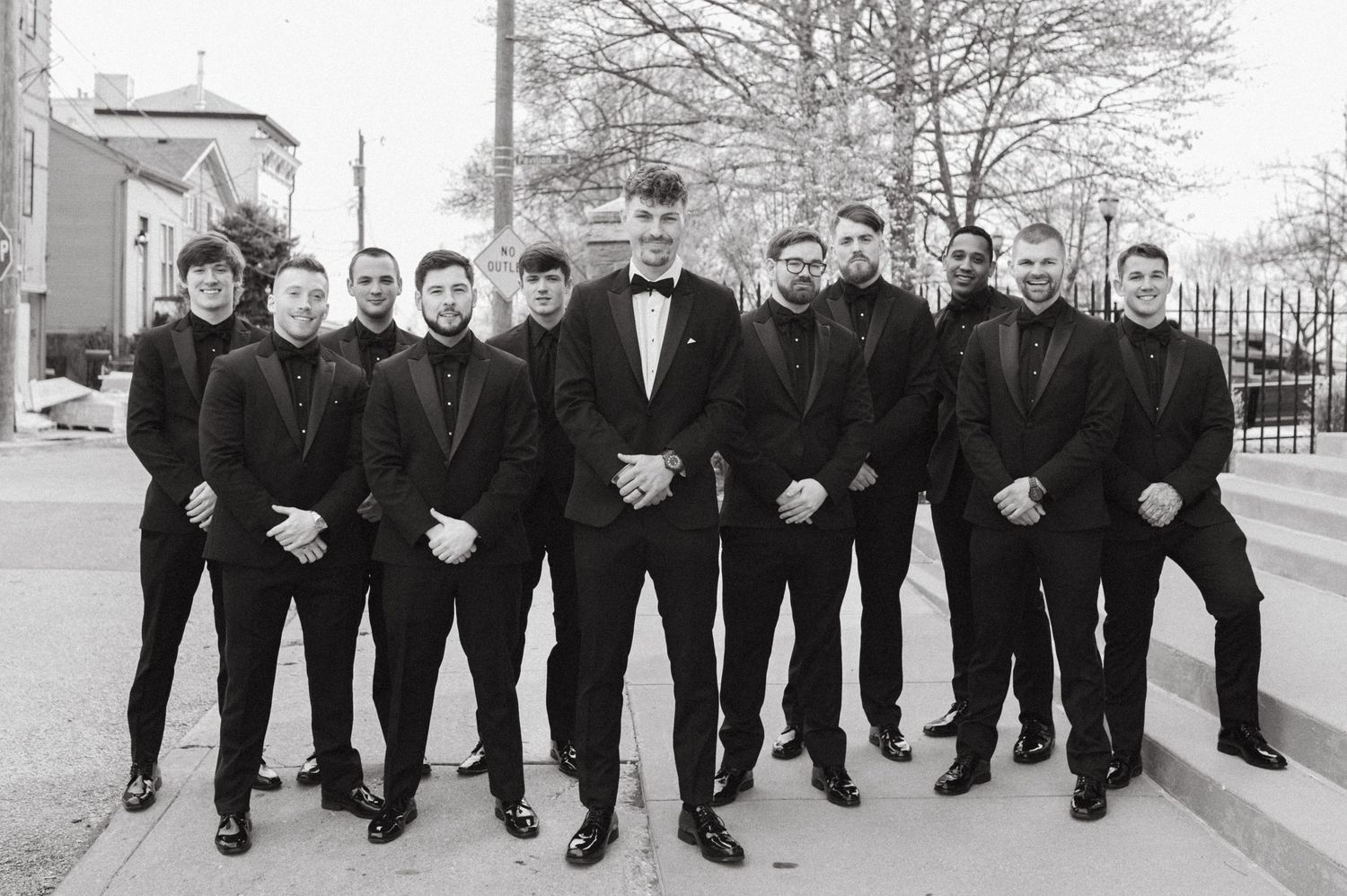 Wedding party of groomsmen in black suits posing together outdoors.