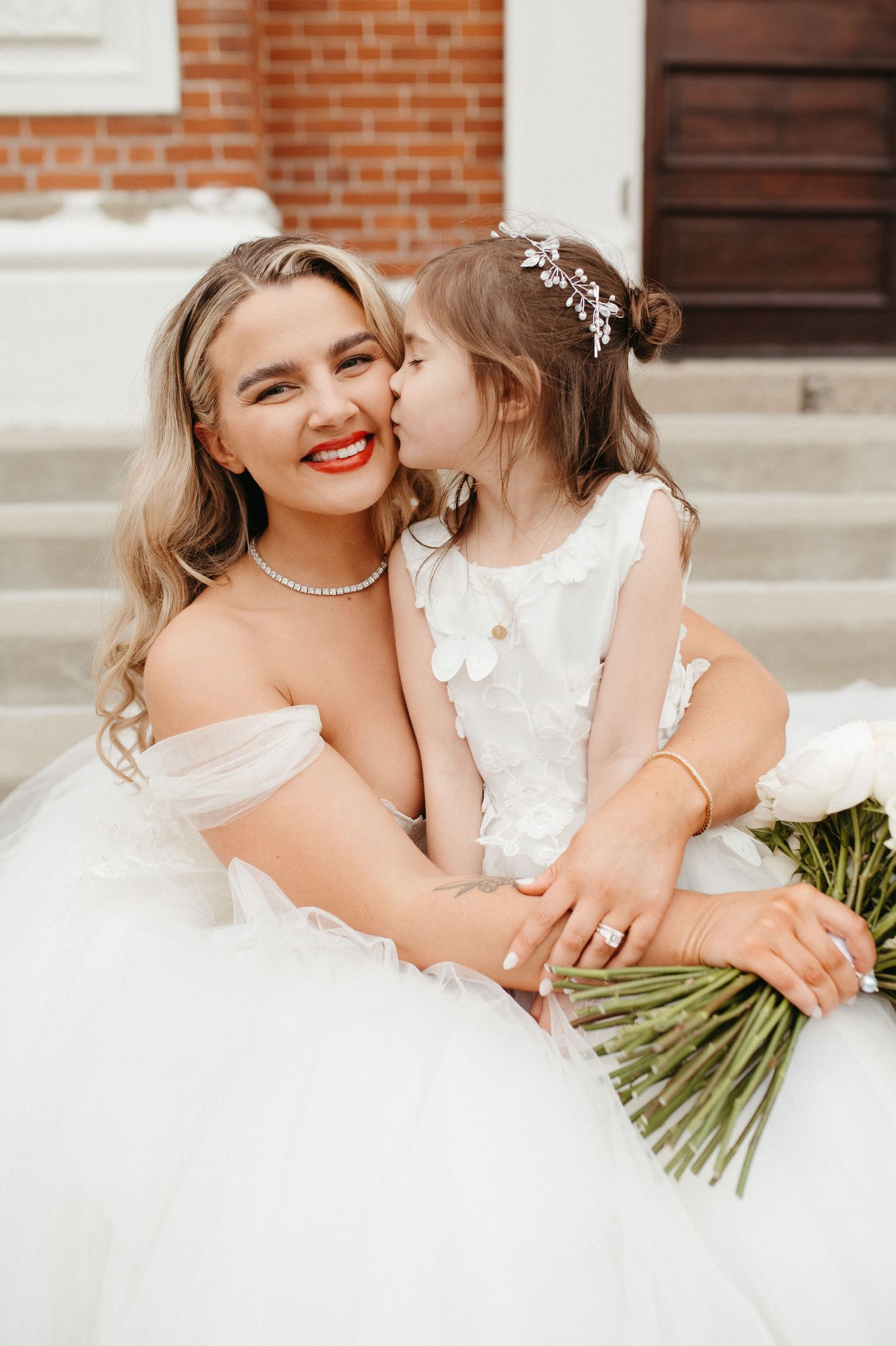 Sweet moment between bride in white gown and flower girl on wedding day.