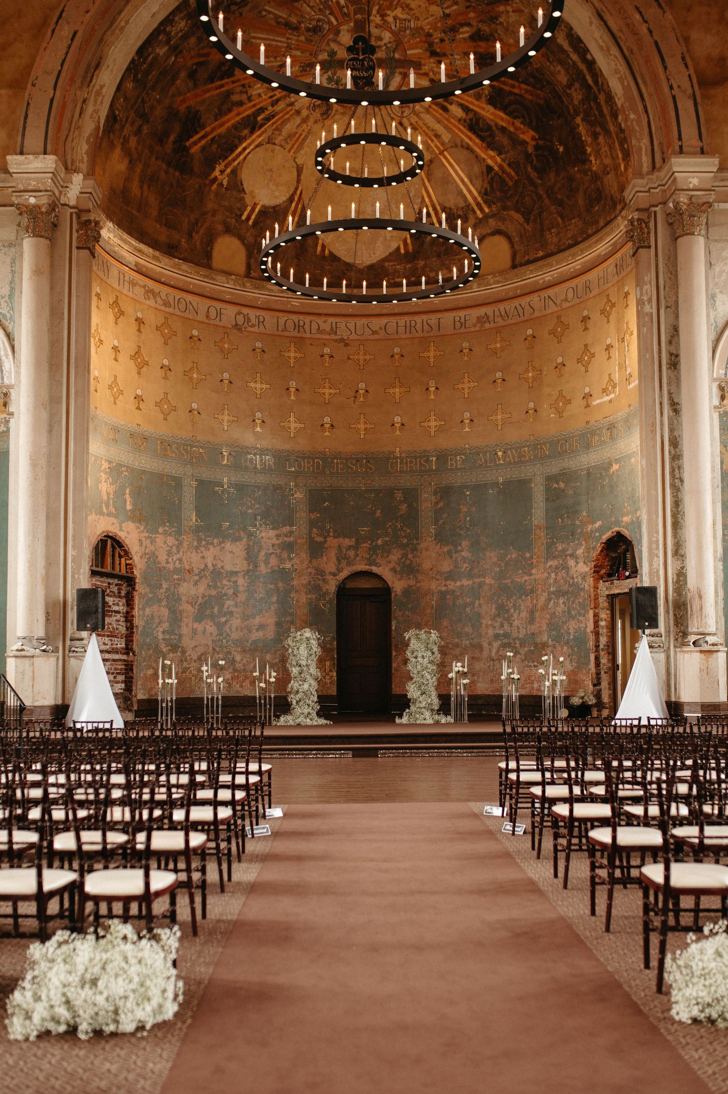 Grand historic venue with arched ceiling, chandeliers, and rows of chairs set up for wedding ceremony.