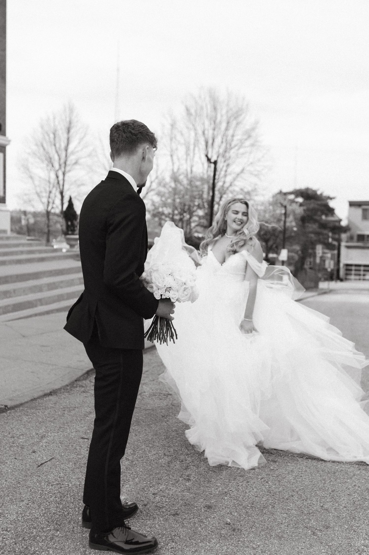 Black and white photo captures romantic moment between newlyweds on church steps.