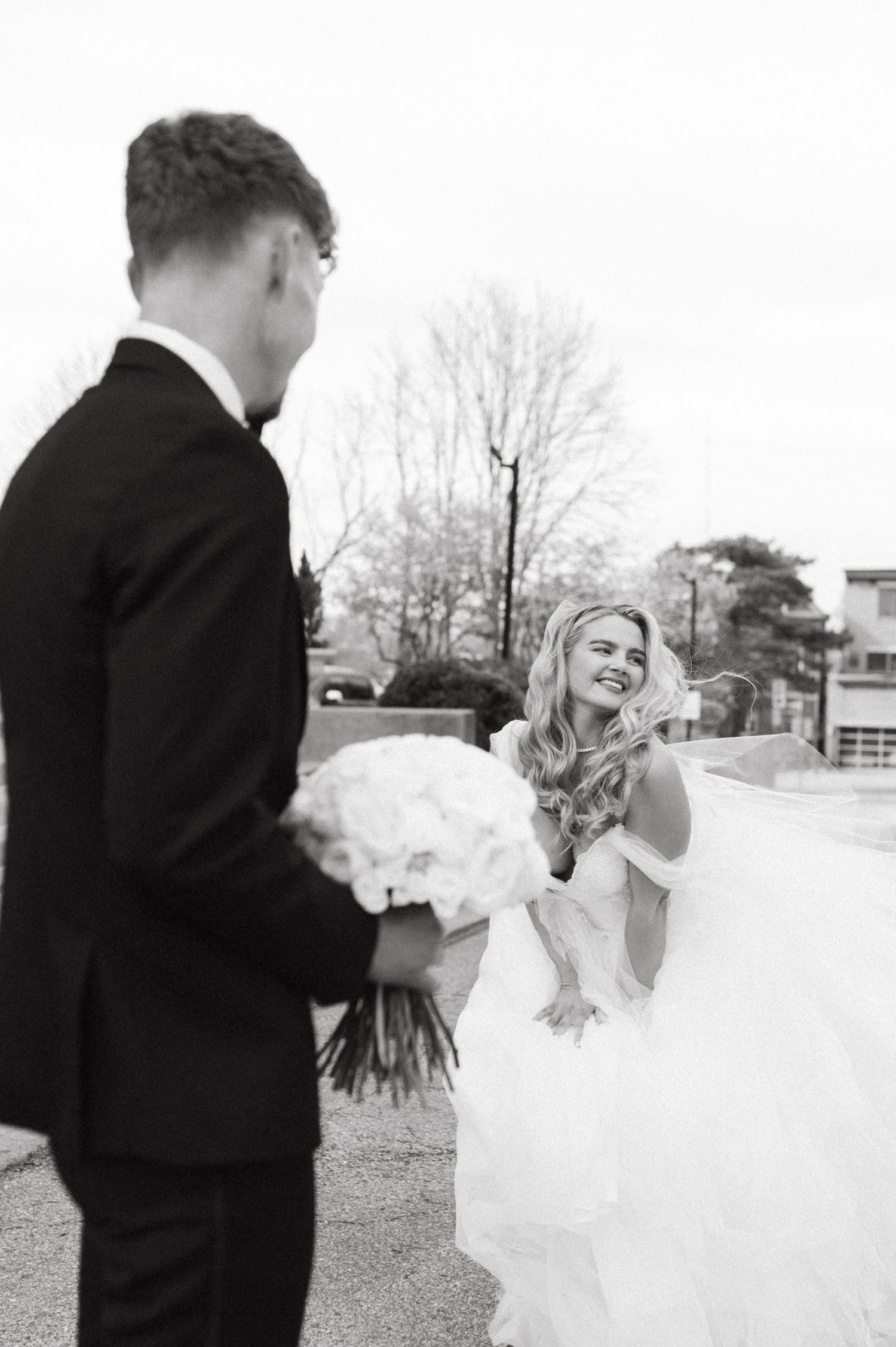 Black and white photo of newlyweds sharing a joyful moment with a bouquet of white flowers.