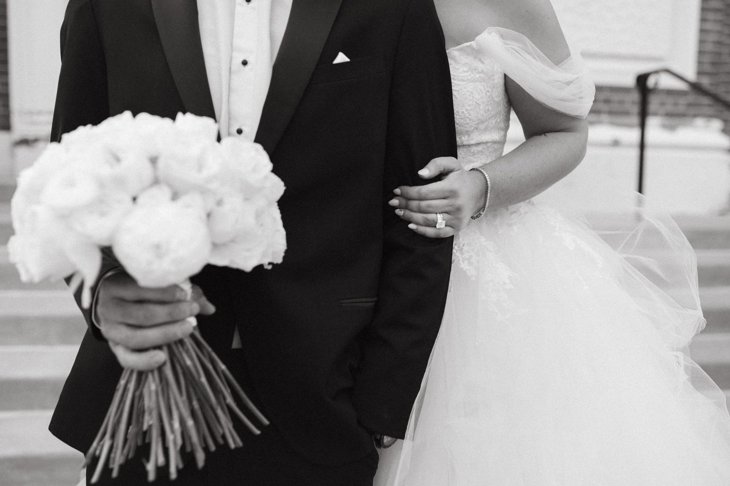 Close-up of bride and groom holding white flower bouquet in formal wedding attire.