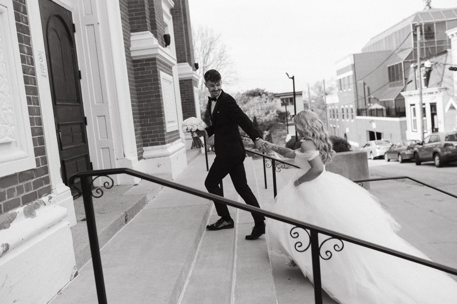 Playful wedding couple on church steps in black and white photography.