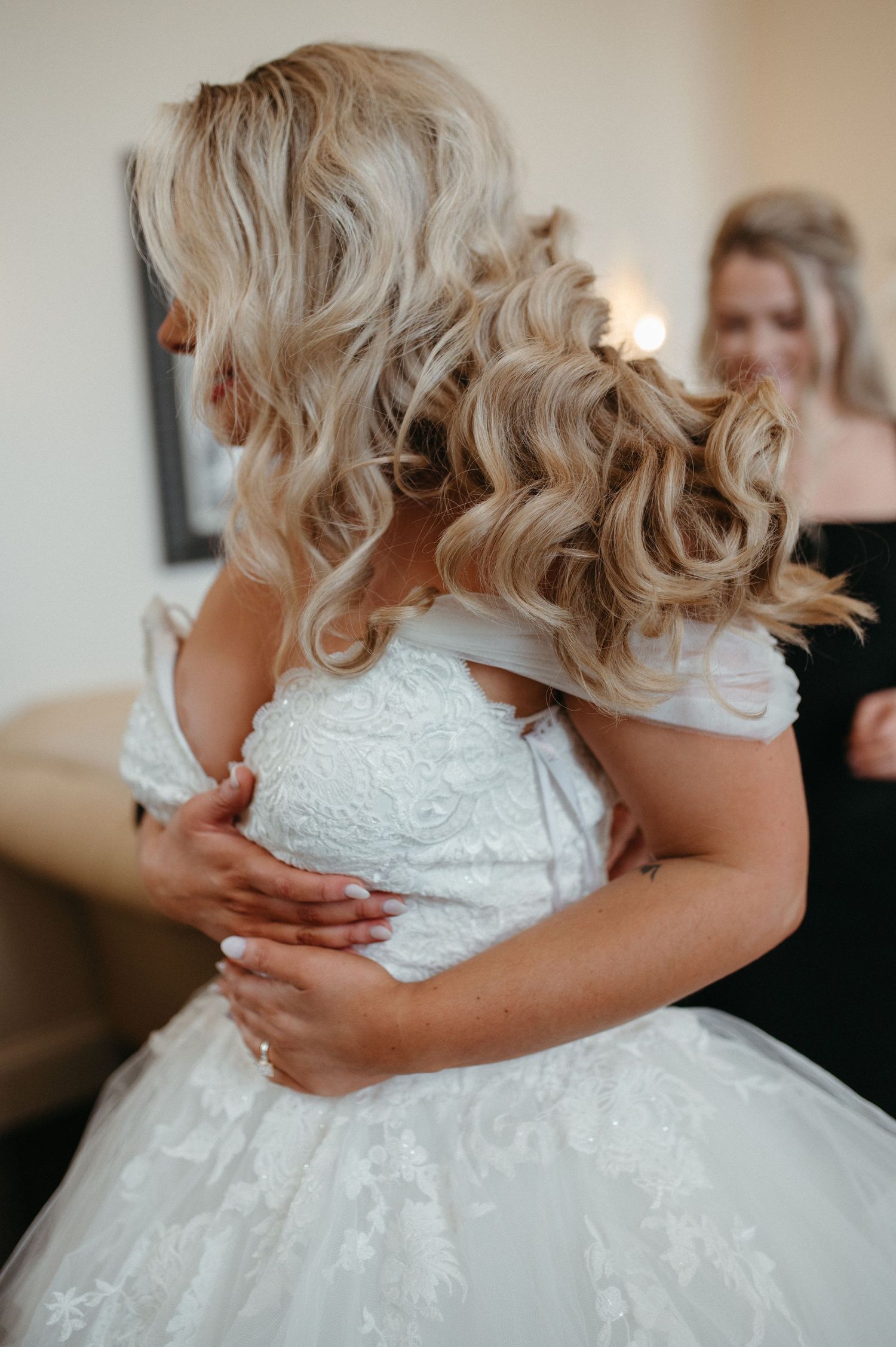 Close-up of intricate lace detailing on a white wedding dress with soft curled hairstyling.