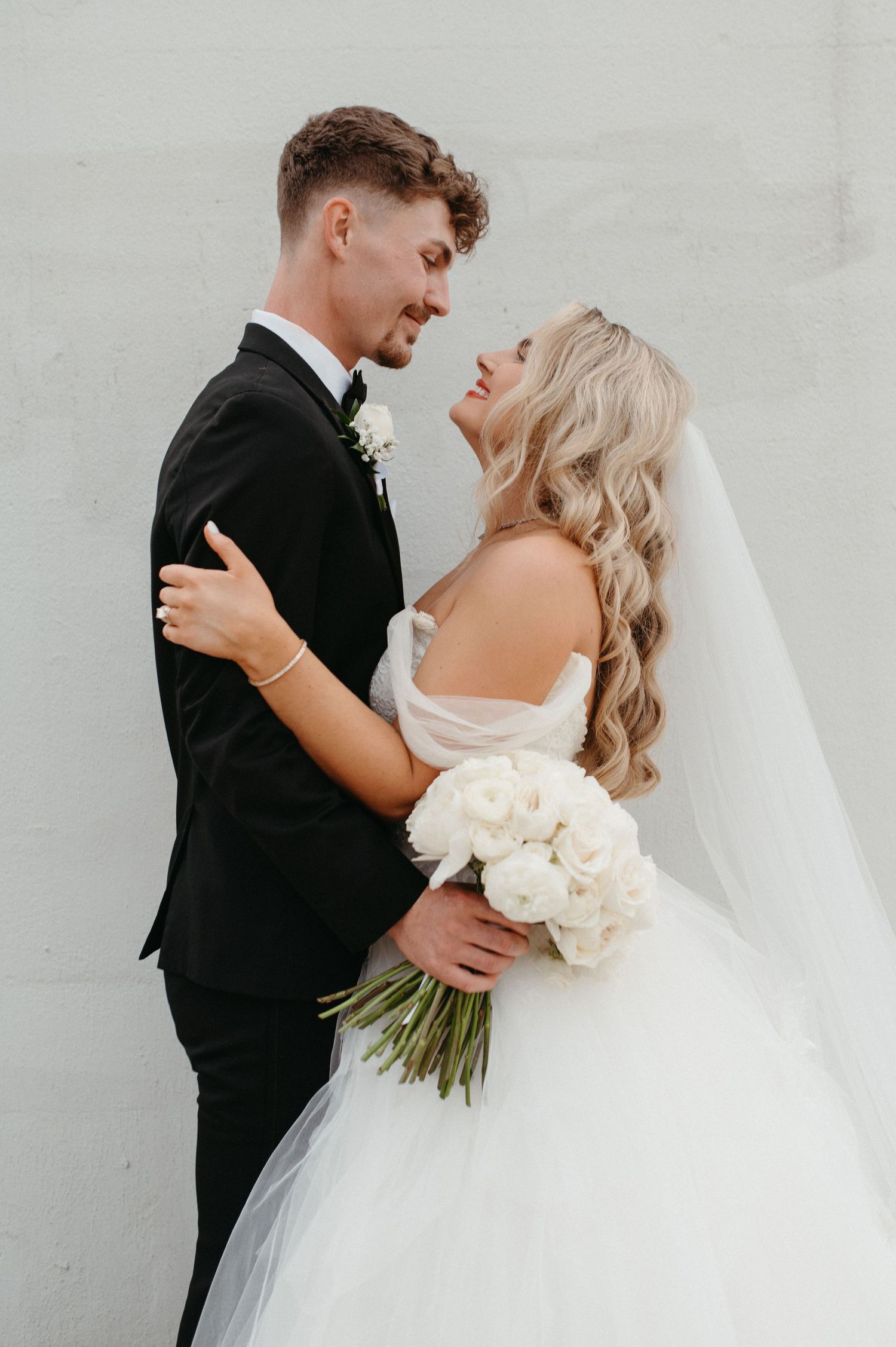 Romantic wedding portrait of couple embracing with white floral bouquet.