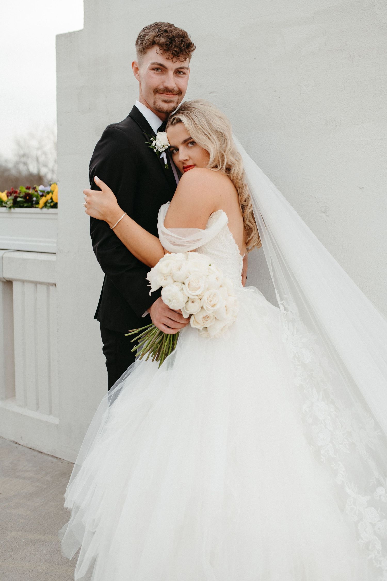Intimate wedding portrait with couple embracing against white architectural backdrop.