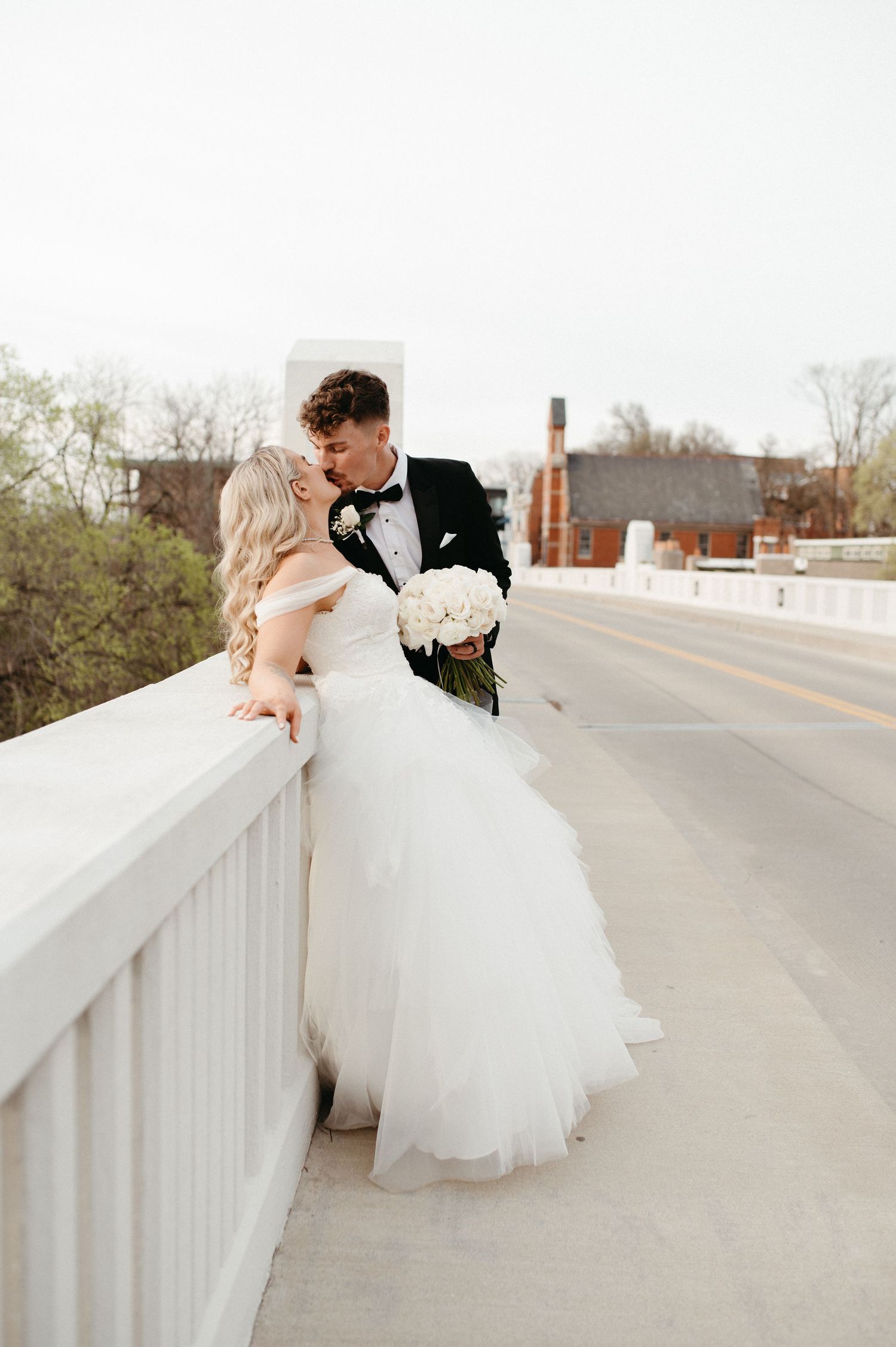 A romantic wedding couple shares an intimate moment on a bridge with white railings.