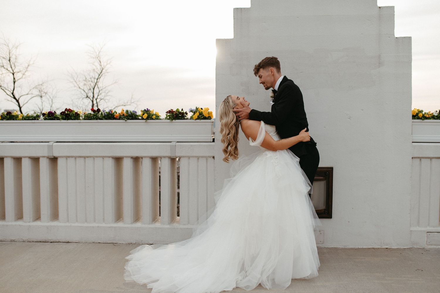 A romantic wedding portrait against a white architectural backdrop at sunset.