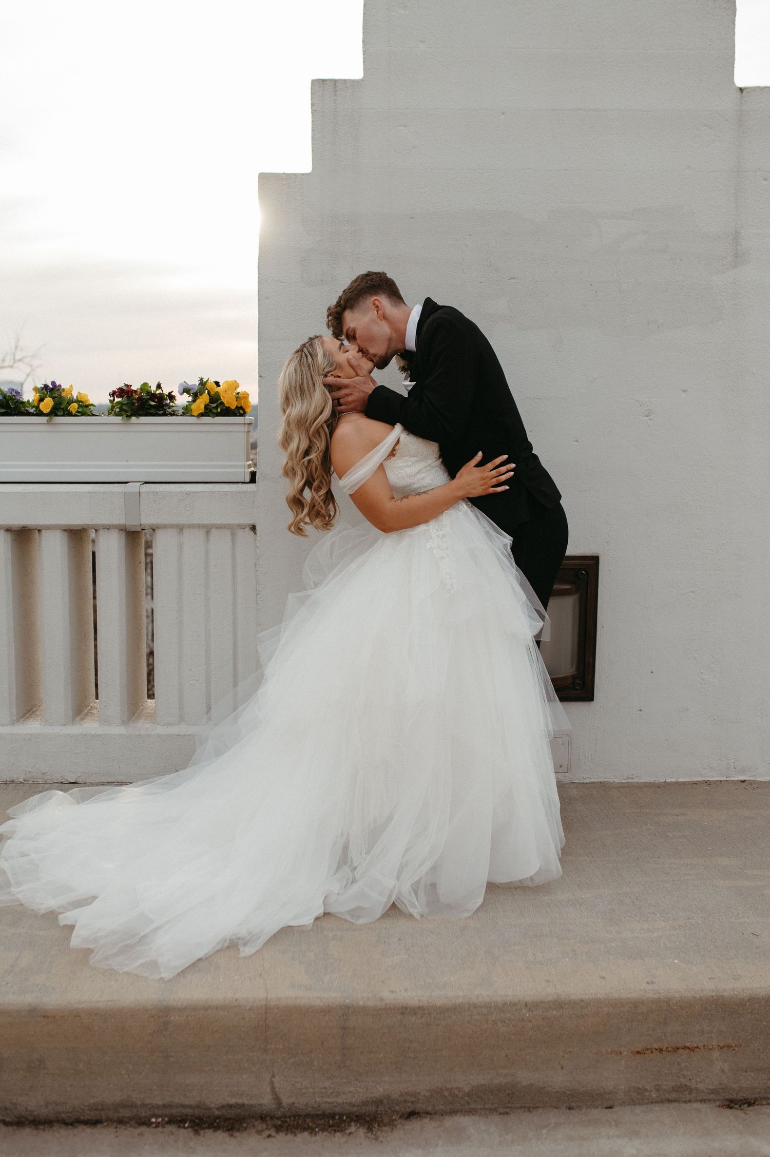 A romantic dip kiss between newlyweds against a white architectural background.