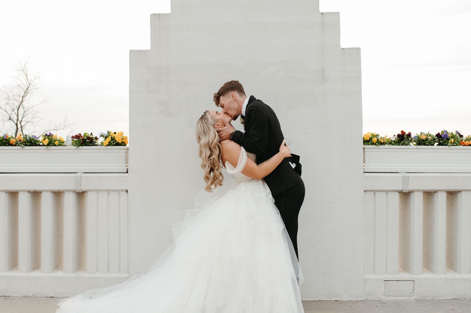 A joyful wedding couple embraces against a white architectural backdrop.