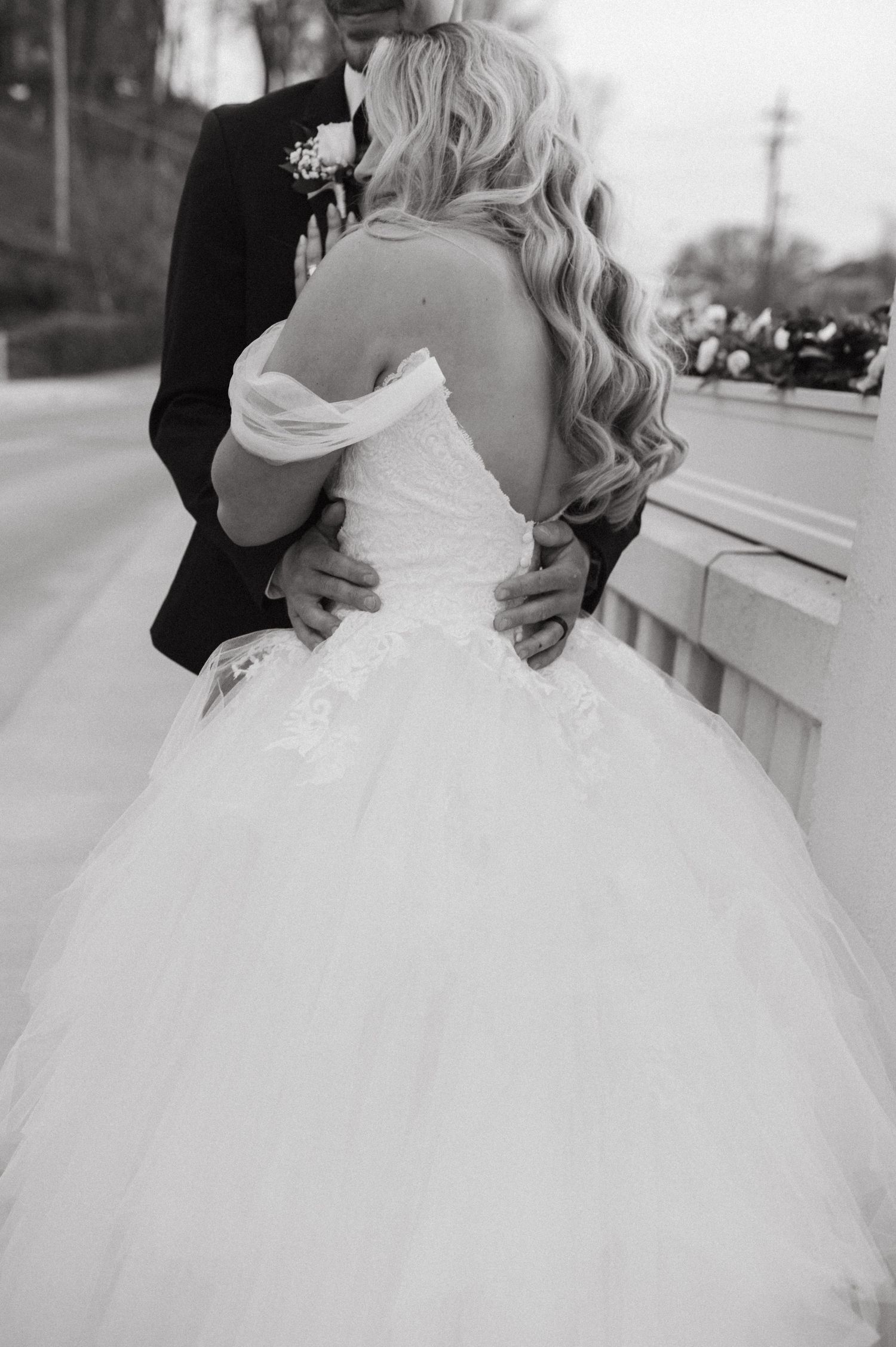 A black and white close-up of a bride in a voluminous tulle gown being embraced from behind.