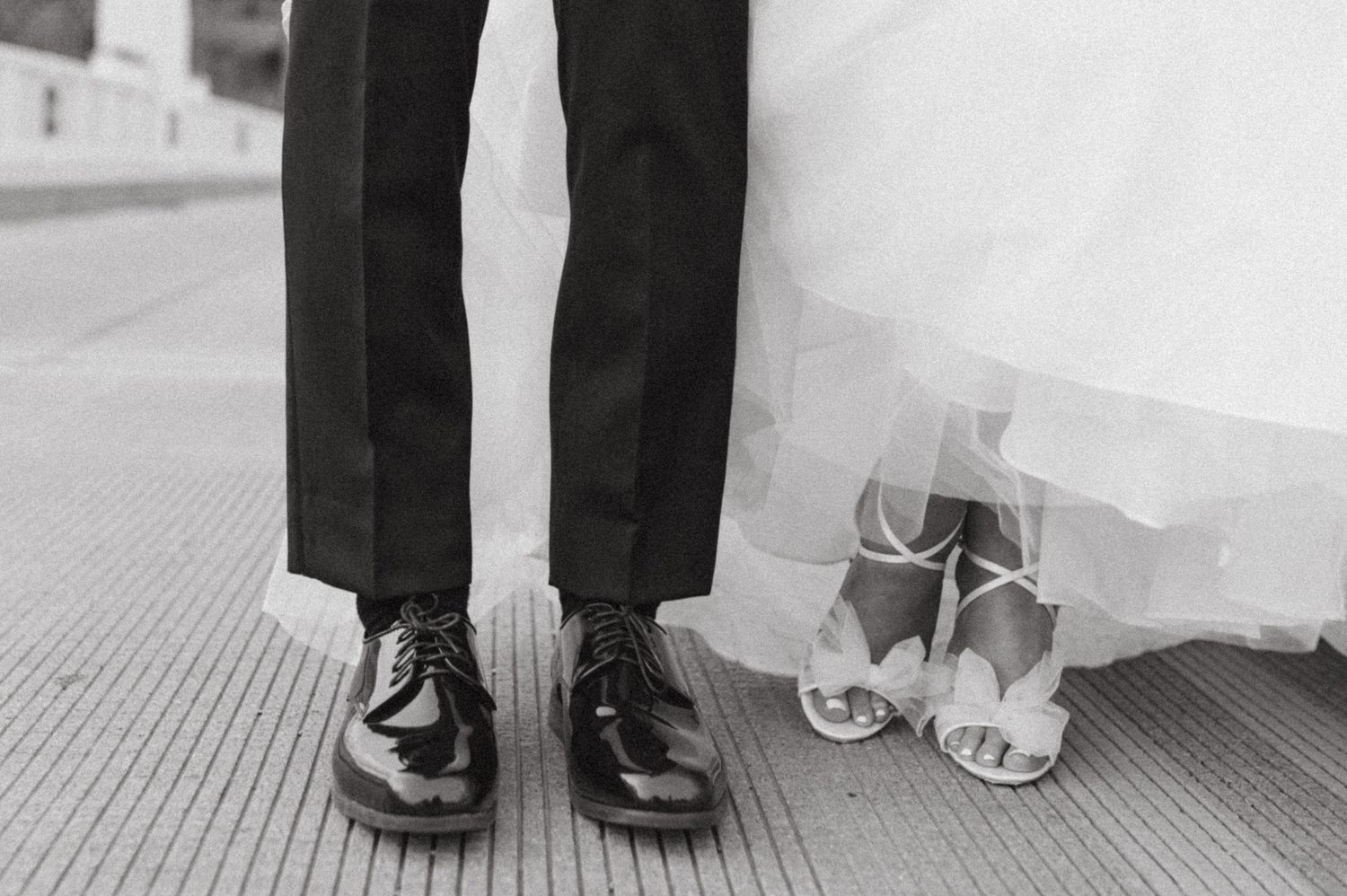 A black and white detail shot of wedding shoes showing formal dress shoes next to bridal heels.