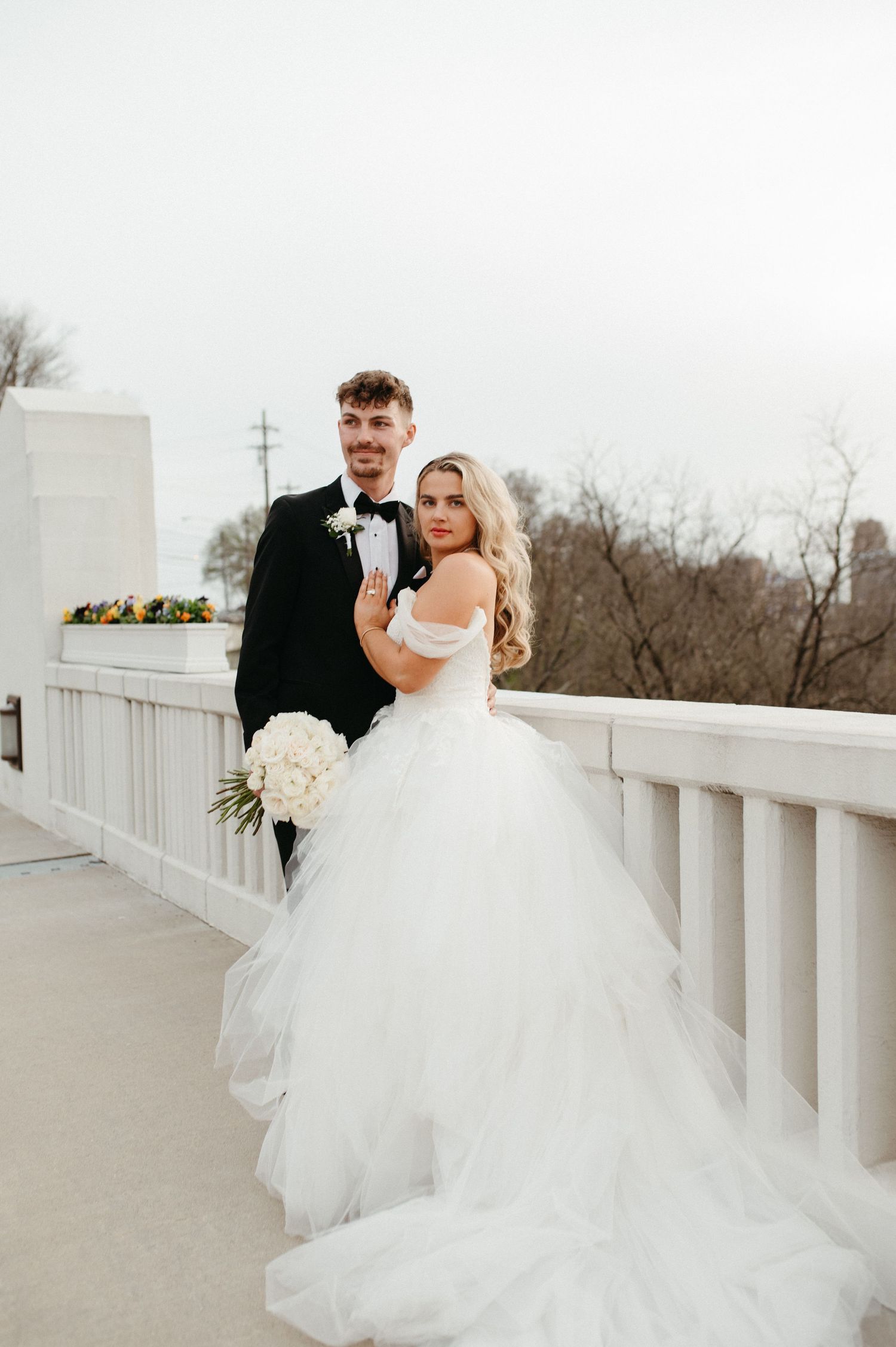 An elegant wedding couple poses against white railings with a dramatic tulle wedding gown.