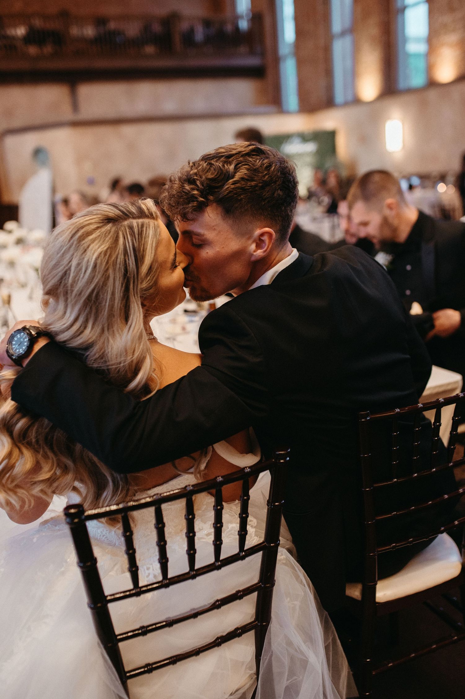 Intimate wedding reception moment showing a couple sharing a romantic kiss while seated at their table.