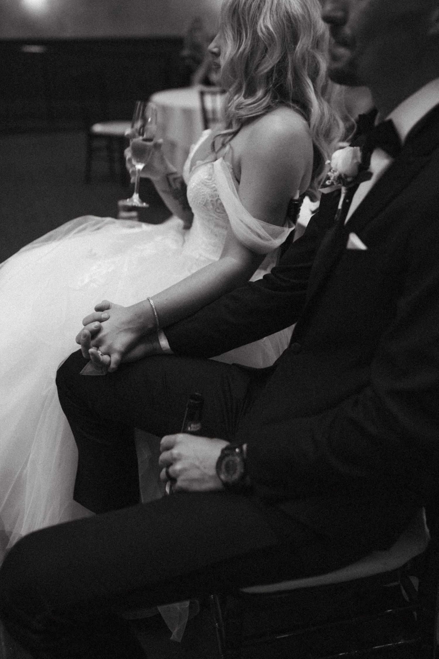 Side view of bride in white gown and groom in black suit seated at wedding reception.