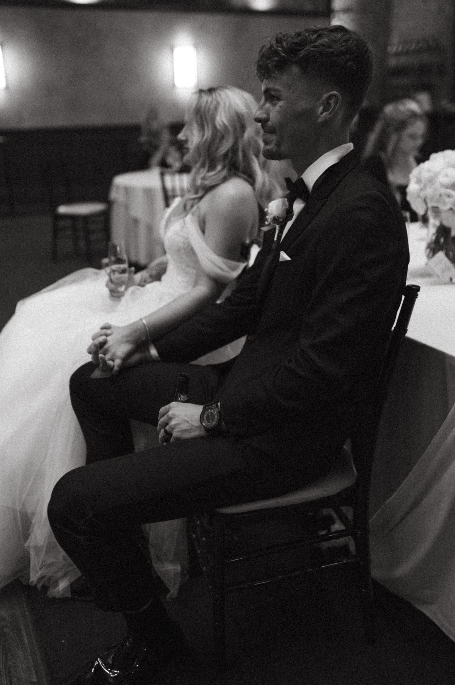 Black and white candid shot of newlyweds sitting together at their reception venue.
