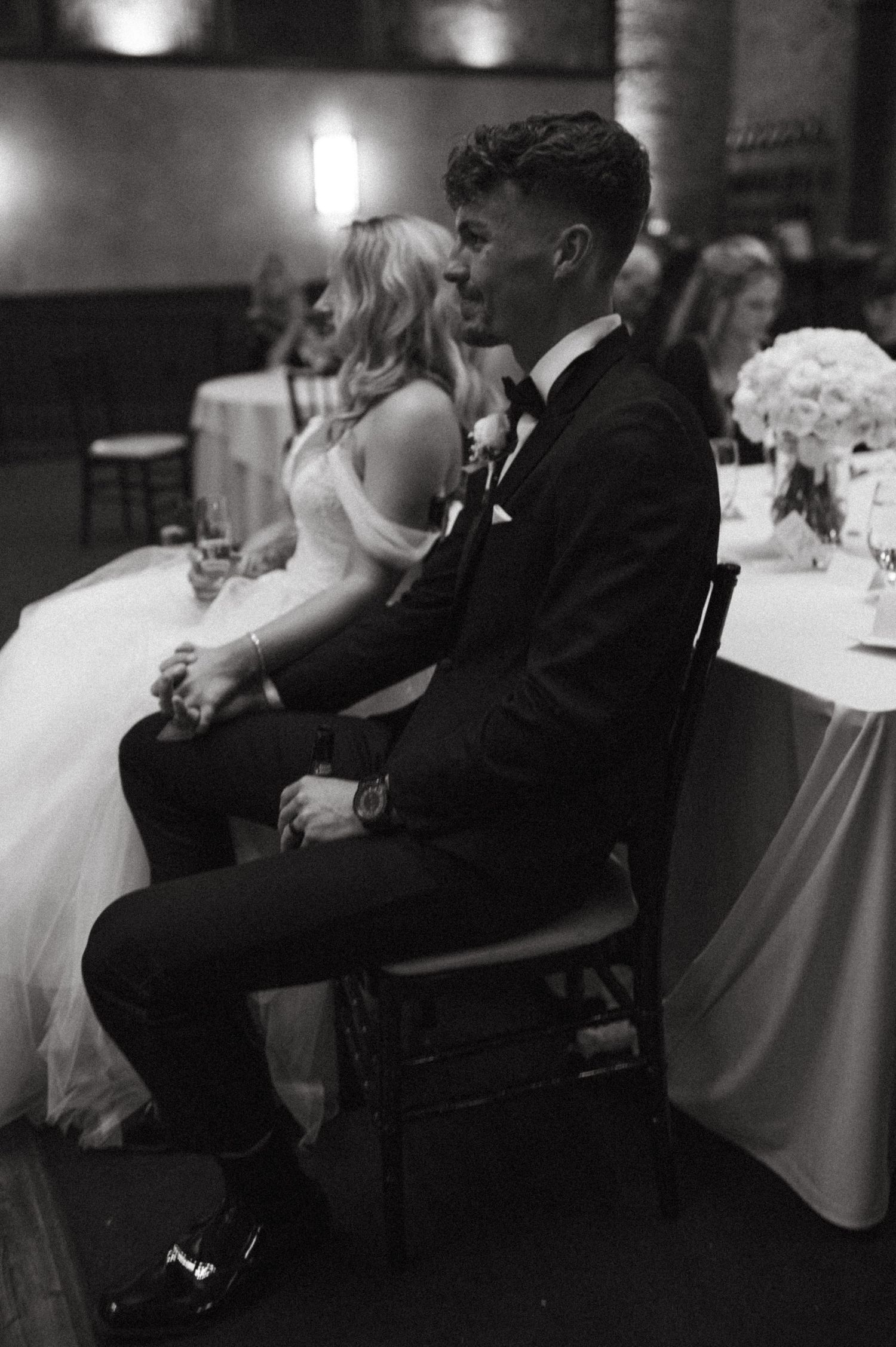 Elegant bride and groom seated at their reception table in formal wedding attire.
