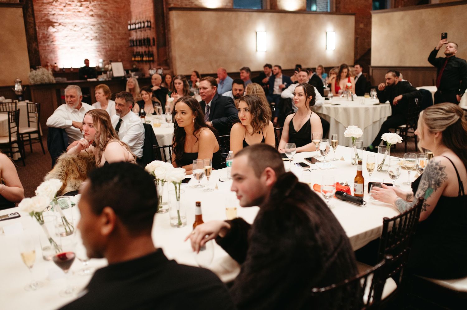 Wedding reception guests seated at round tables in rustic brick venue.