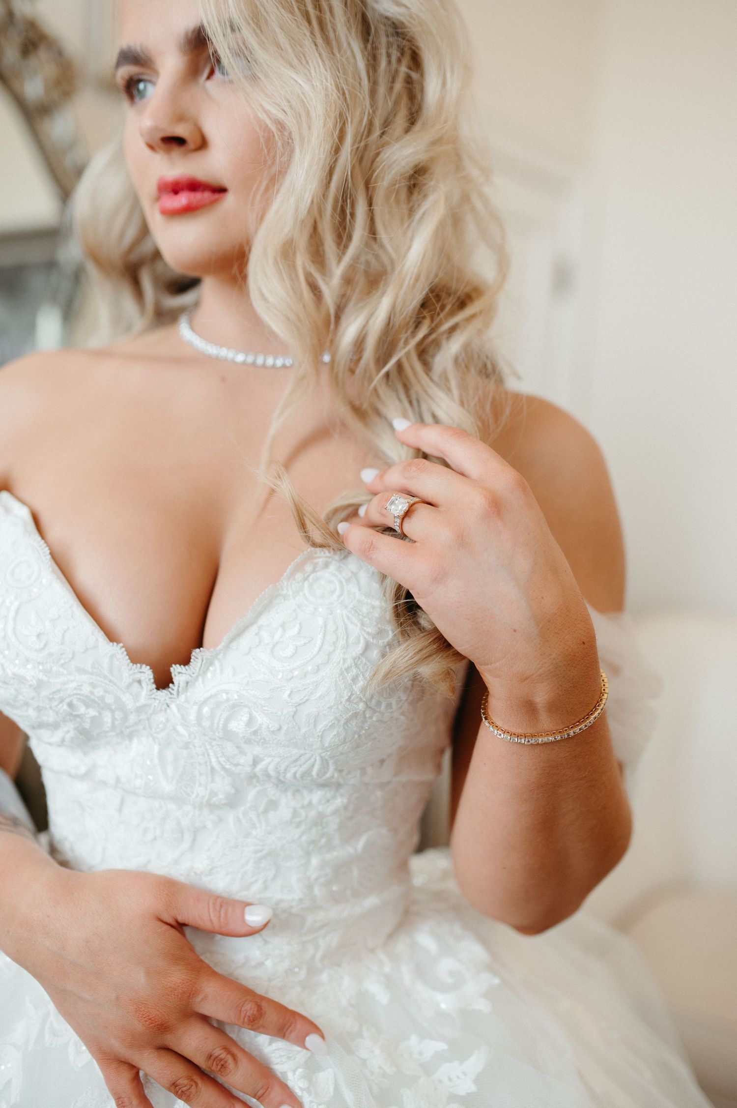 Detail shot of bridal accessories including pearl necklace and engagement ring with lace dress.