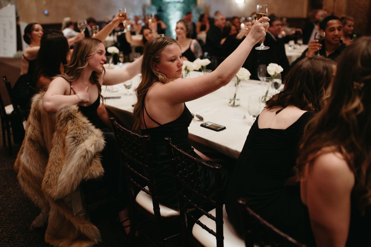 Wedding guests raising their glasses during a celebratory toast at reception.