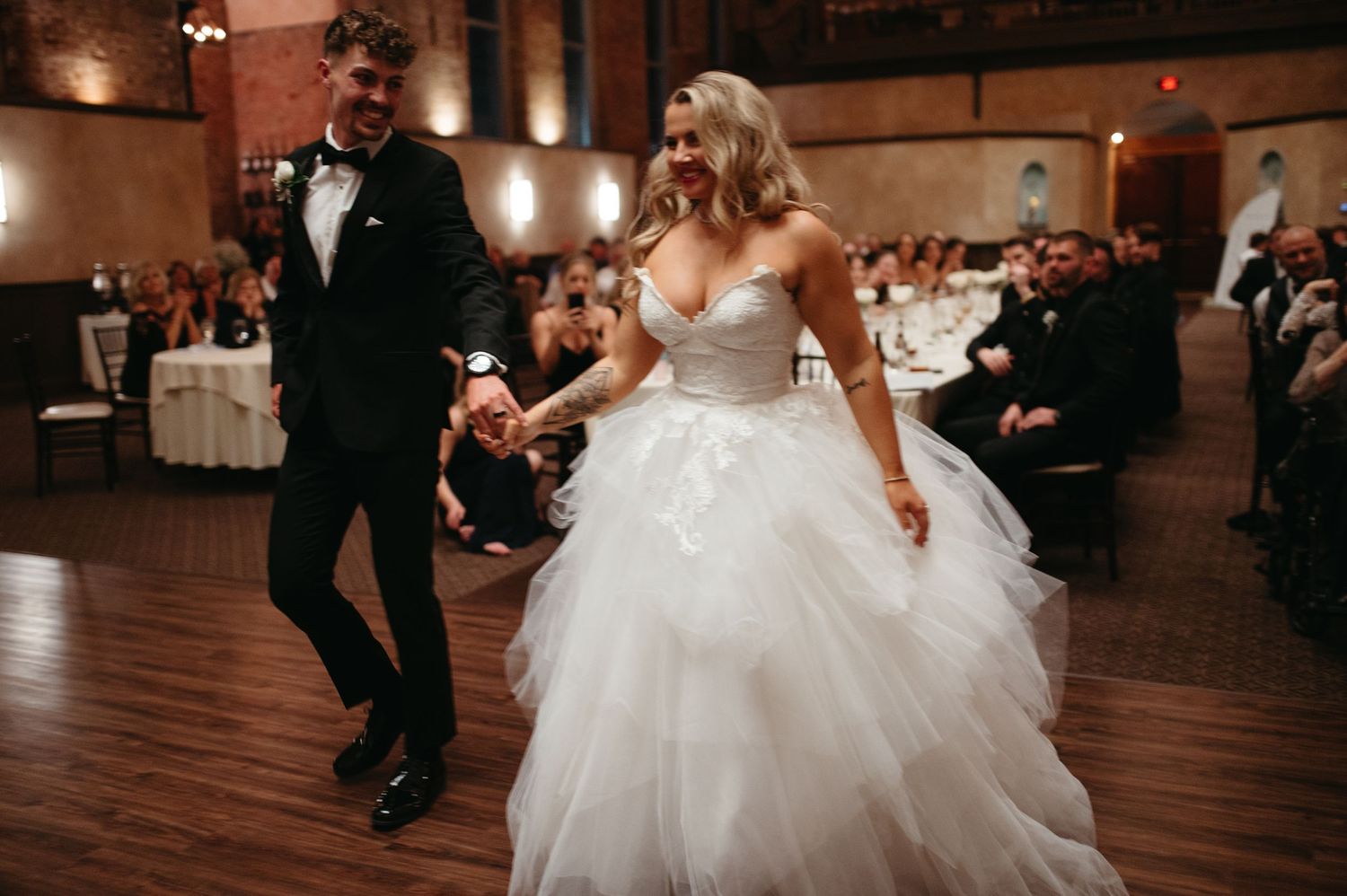 A couple dances together during their wedding reception in a venue with warm lighting and wooden floors.