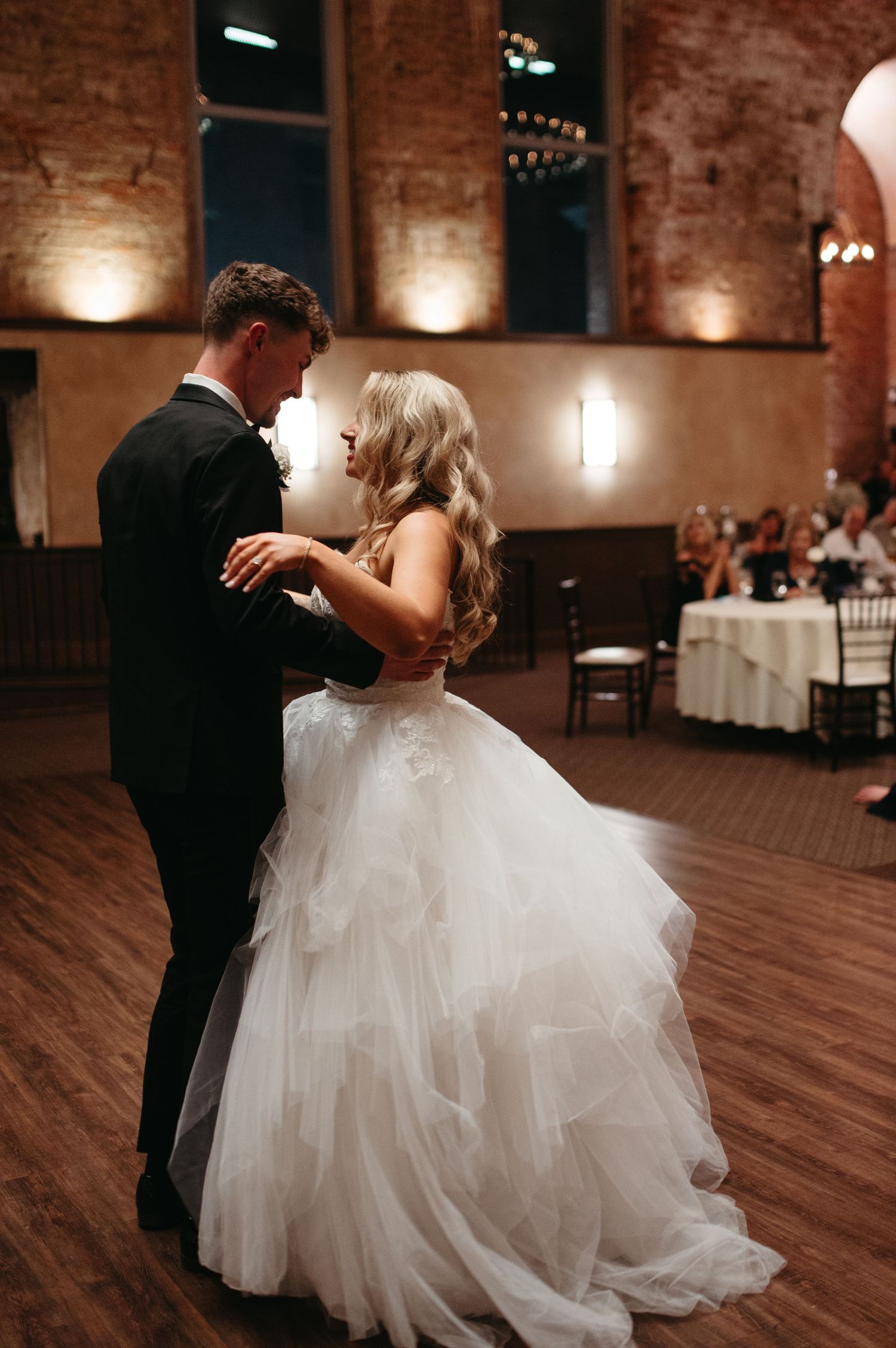 A romantic moment between newlyweds dancing in an elegant brick-walled reception venue.