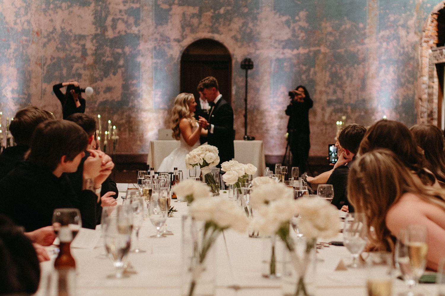 A wedding reception dinner scene with elegant table settings and ambient lighting in a rustic venue.