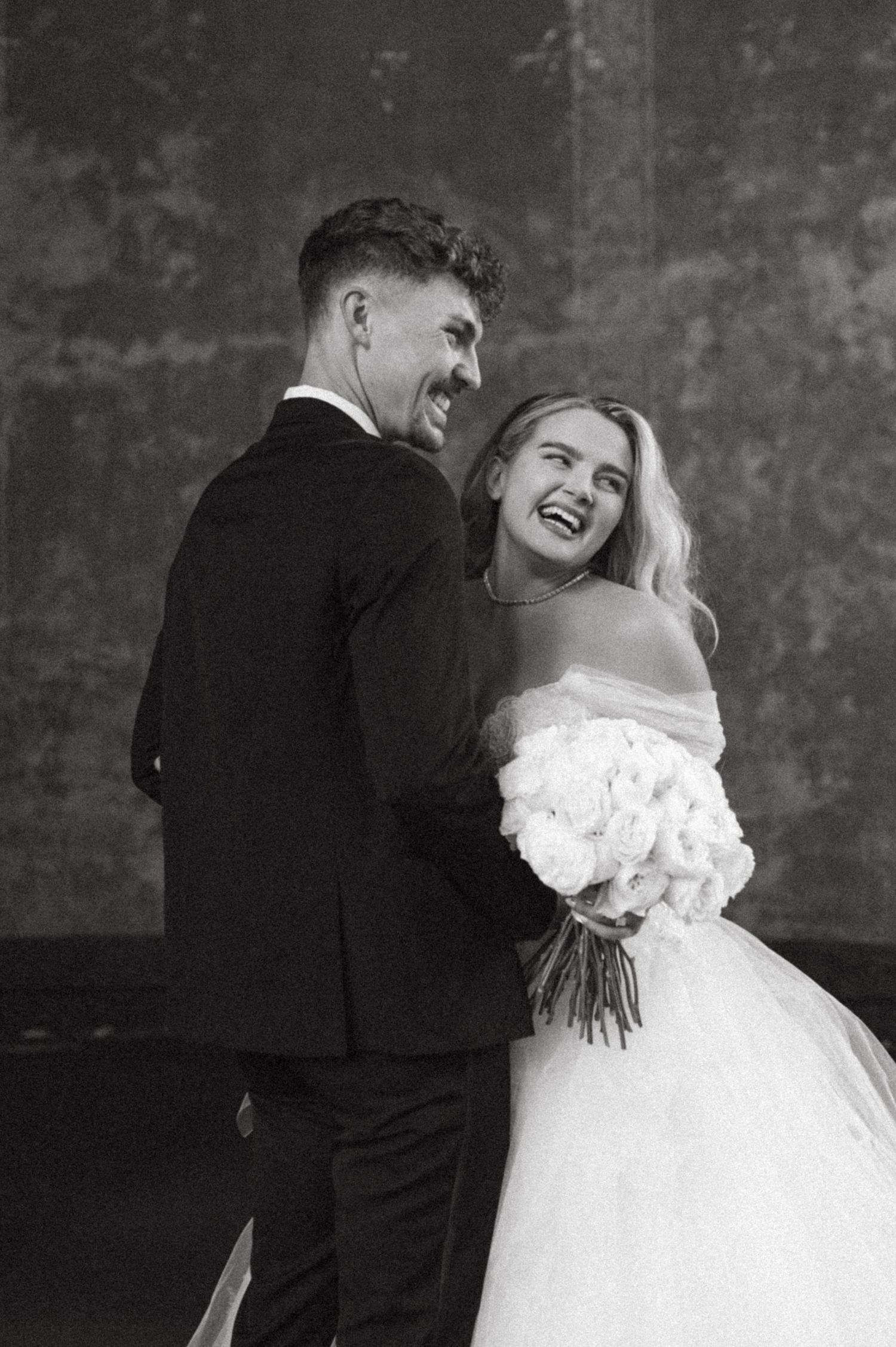 A joyful black and white wedding portrait capturing the newlyweds sharing a candid laughing moment.