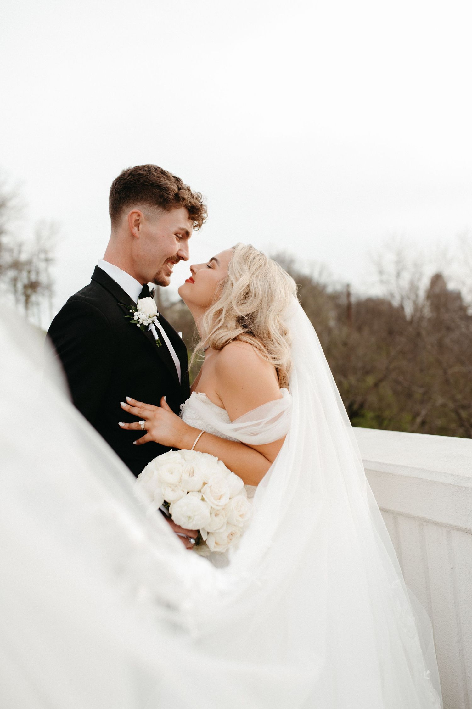 A romantic wedding portrait showcasing the couple's intimate moment with flowing veil in the foreground.