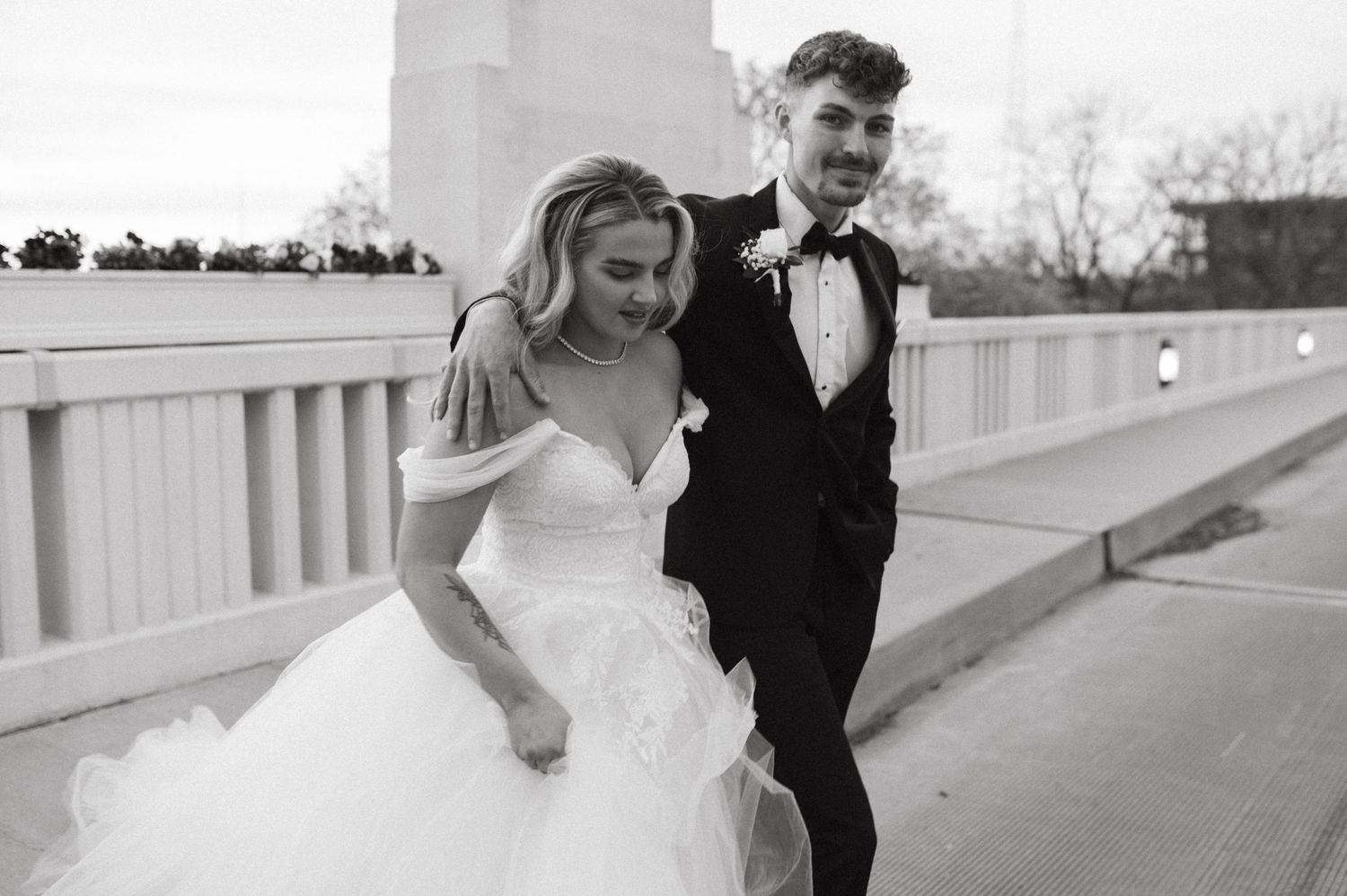 A candid wedding photo of the couple walking along a white railed pathway in formal attire.