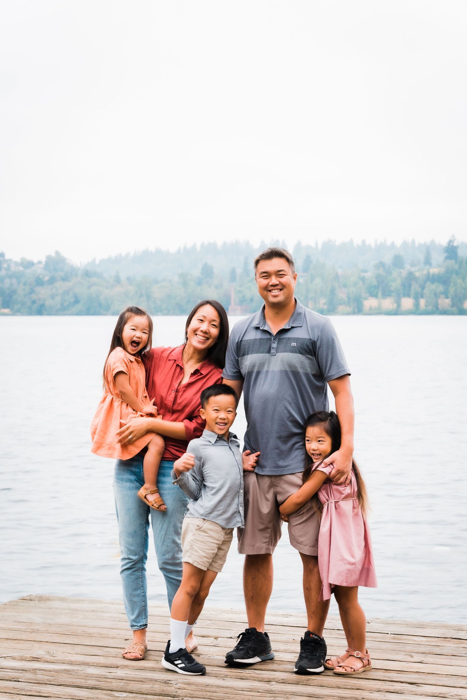 A joyful family poses together on a wooden dock by a scenic lake on a peaceful day.