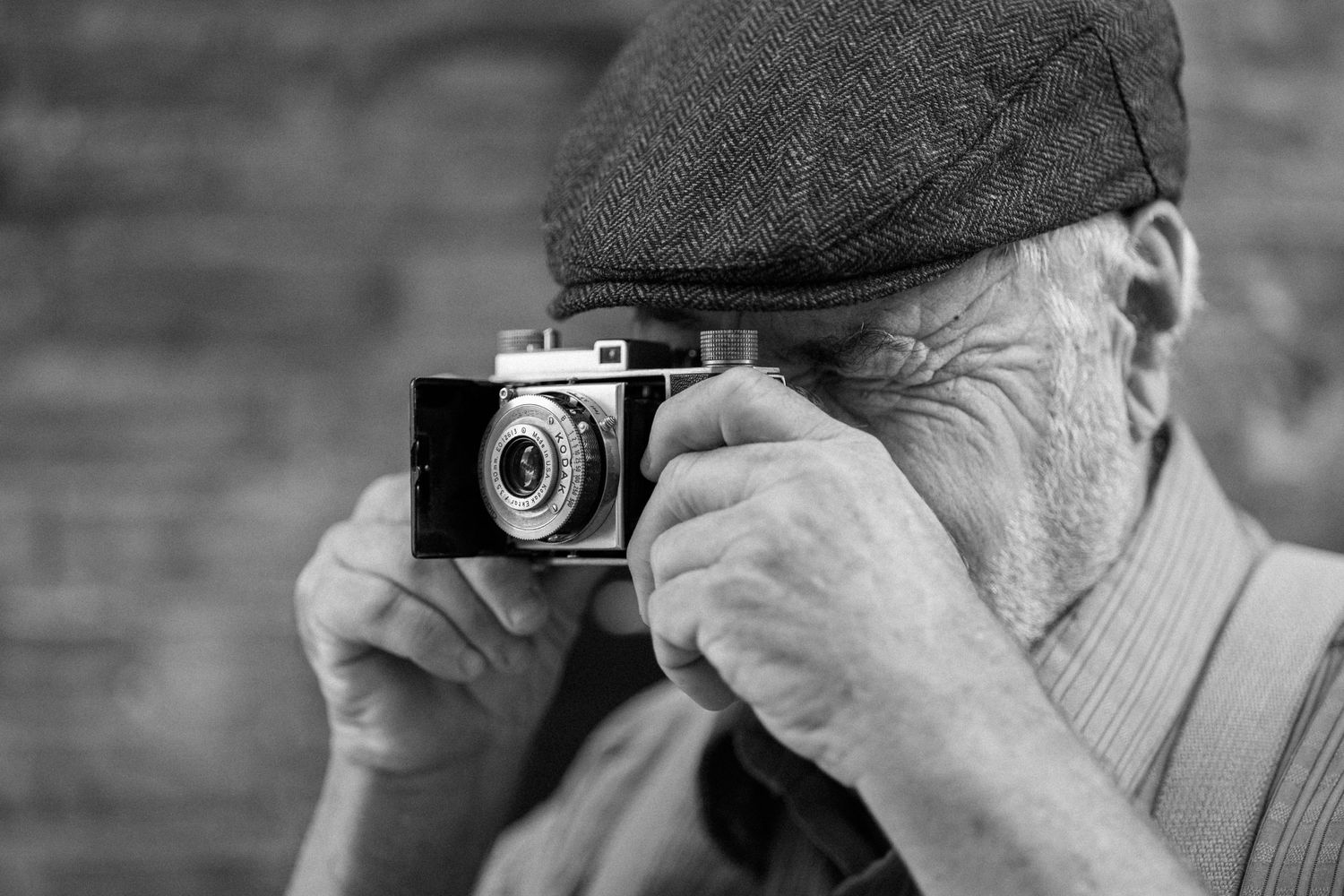 older man with cap taking photo with vintage camera