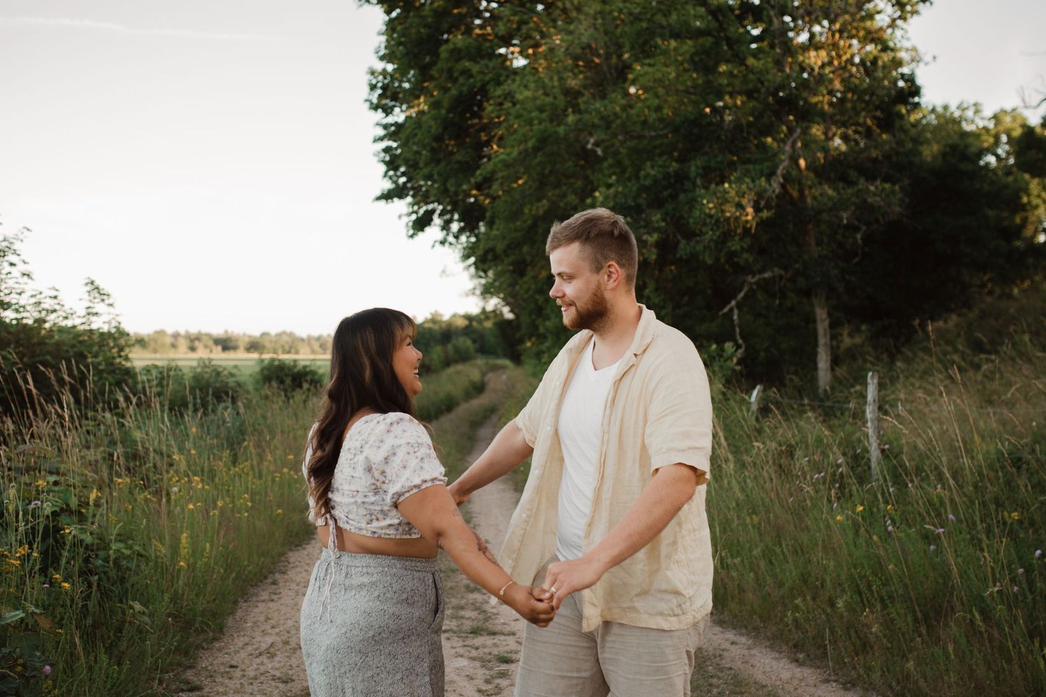 Couple sharing an intimate moment on a dirt path surrounded by tall grass at sunset.
