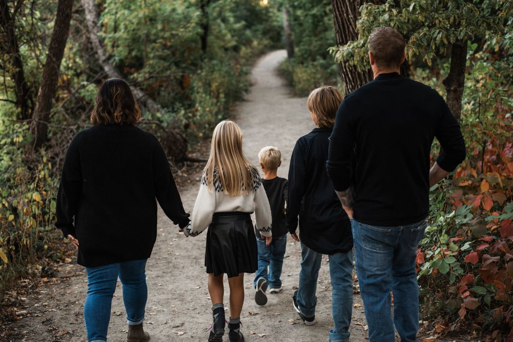 A family walks together holding hands on a tree-lined path during an autumn day.