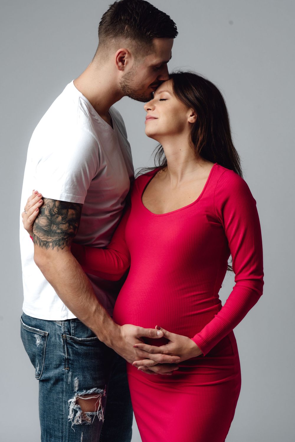 Maternity photo series showing couple embracing in white shirt and red dress.