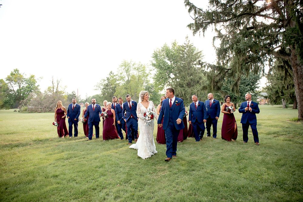 A wedding party walking across a green lawn in navy and burgundy attire.
