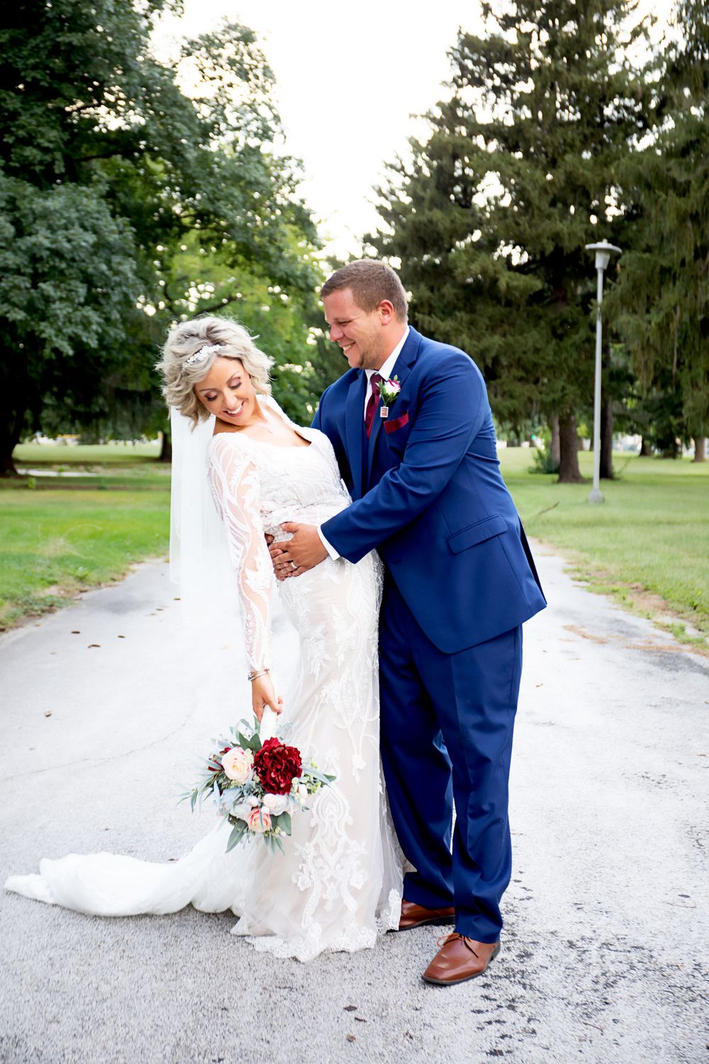 Romantic wedding couple sharing playful moment on garden path with lace dress and navy suit.