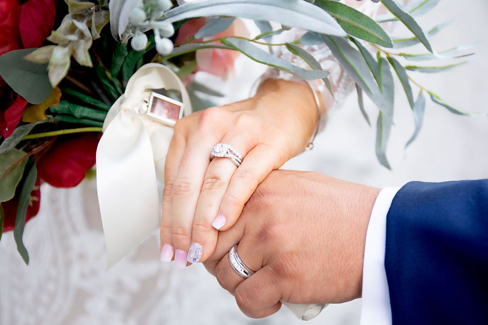 Wedding rings and hands displayed with burgundy floral bouquet details.