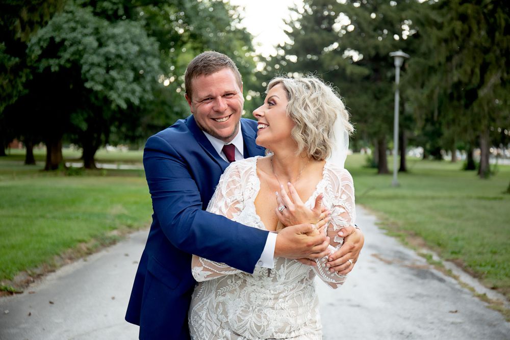 Candid moment of couple laughing together on garden pathway during wedding photoshoot.