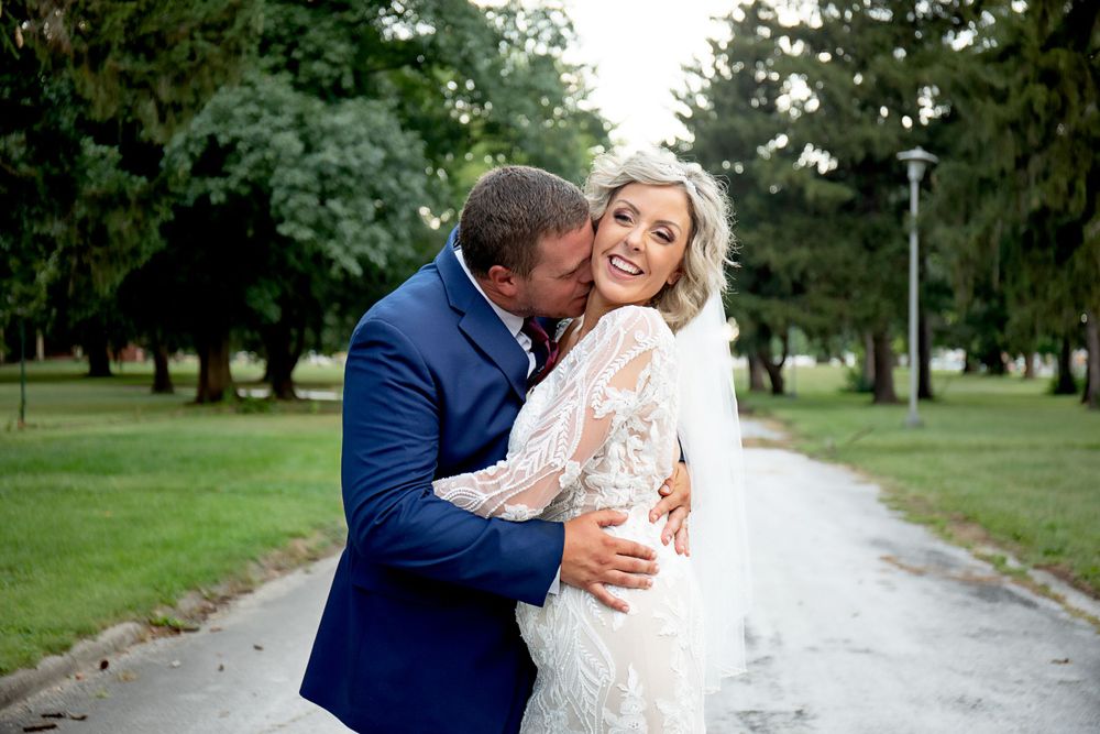 Intimate wedding moment captured on tree-lined path with couple embracing and laughing.