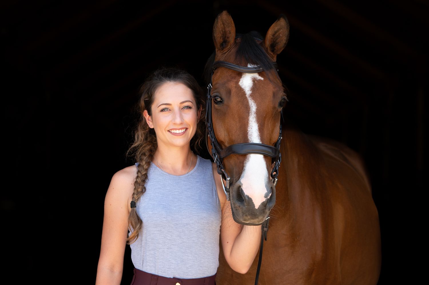 A beautiful bay horse with white markings posing with someone in a stable.