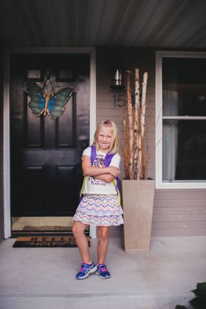 Young child in colorful outfit posing on front porch with butterfly decoration.