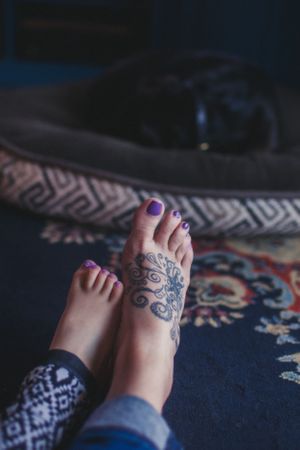 Close-up of feet with purple nail polish and tattoo design resting on patterned fabric.