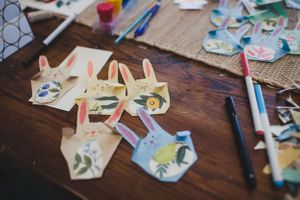 Arts and crafts supplies scattered on wooden table including paper cutouts and markers.